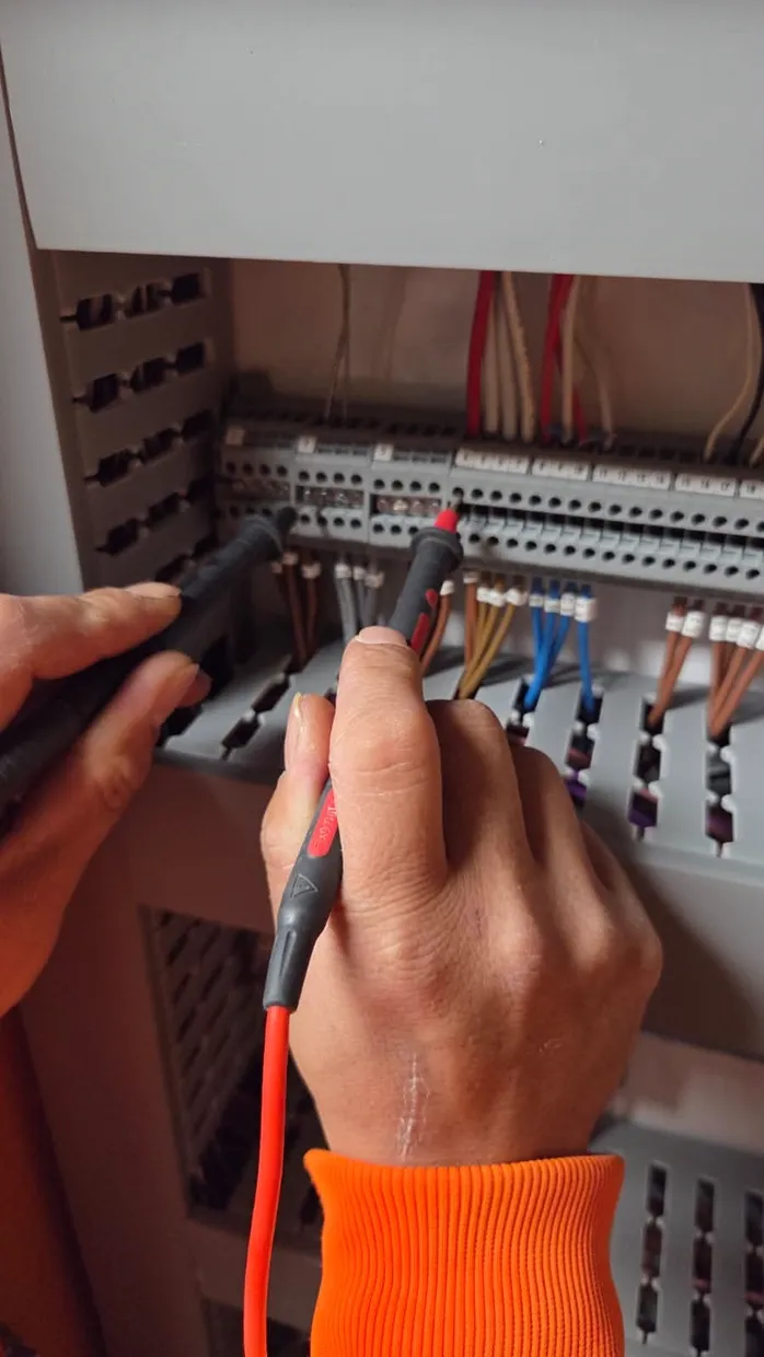 Electrician testing circuits at an open switchboard with a screwdriver