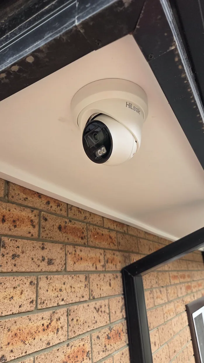 White HiLook CCTV security camera mounted under a soffit beside a brick wall
