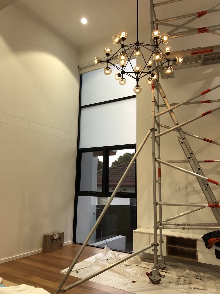 Chandelier being installed from scaffold in a double-height living space