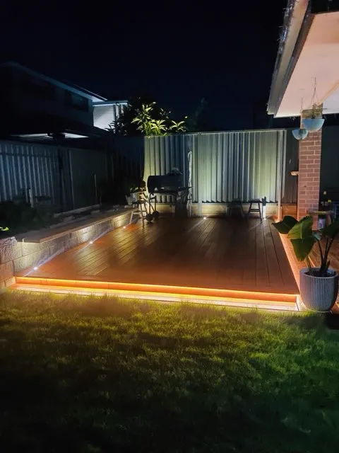 Backyard deck at night lit by a warm strip light running along its edge