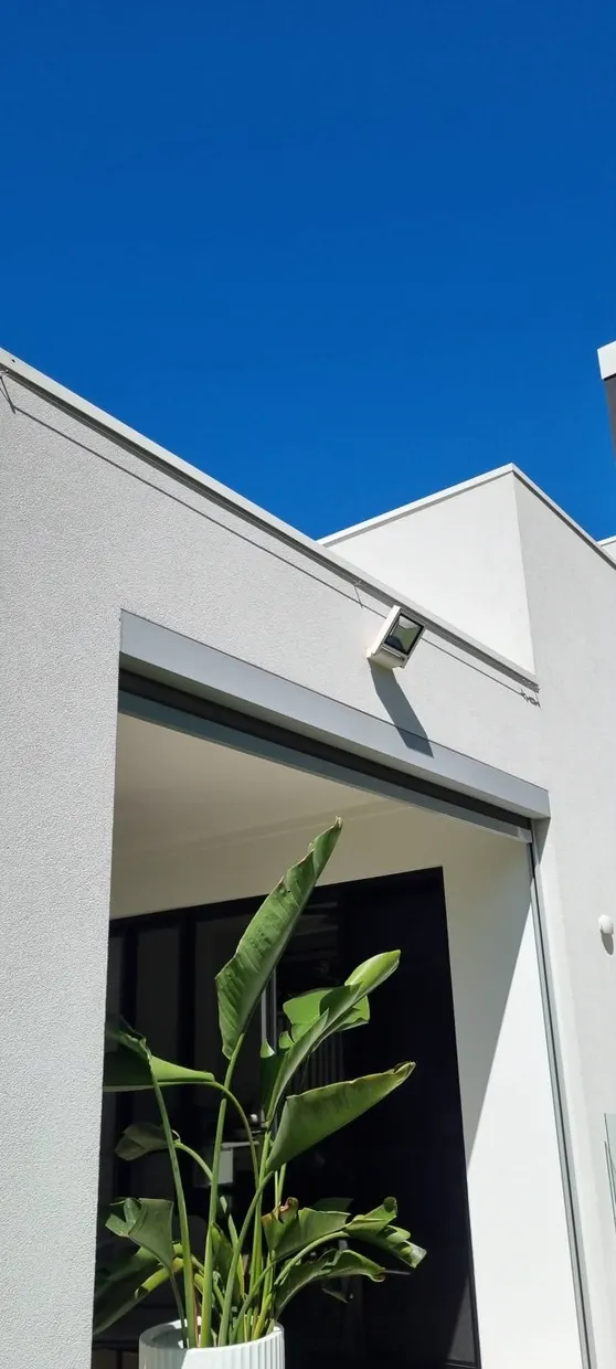 Sensor floodlight mounted high on the external wall of a rendered house against a clear sky