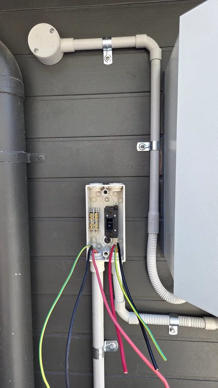 Open weatherproof junction box with terminal block and circuit breaker, coloured conductors mid-installation
