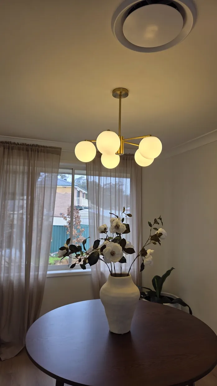 Brass four-globe pendant light with frosted glass shades hanging over a dining table