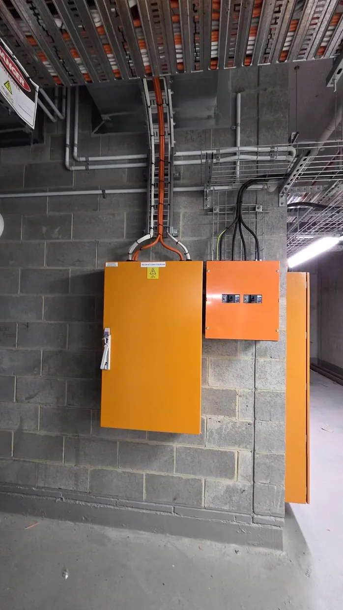 Two orange switchboard enclosures wall-mounted on block work with cable tray and conduit above